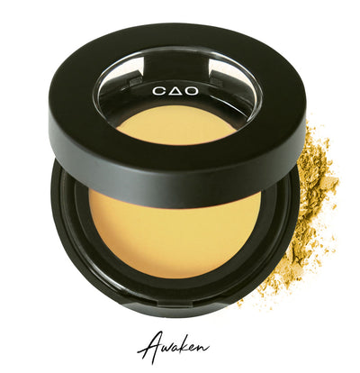 Semi- open eyeshadow compact with yellow eyeshadow in shade "Awaken" compressed powder and on white background with loose eyeshadow powder on white..