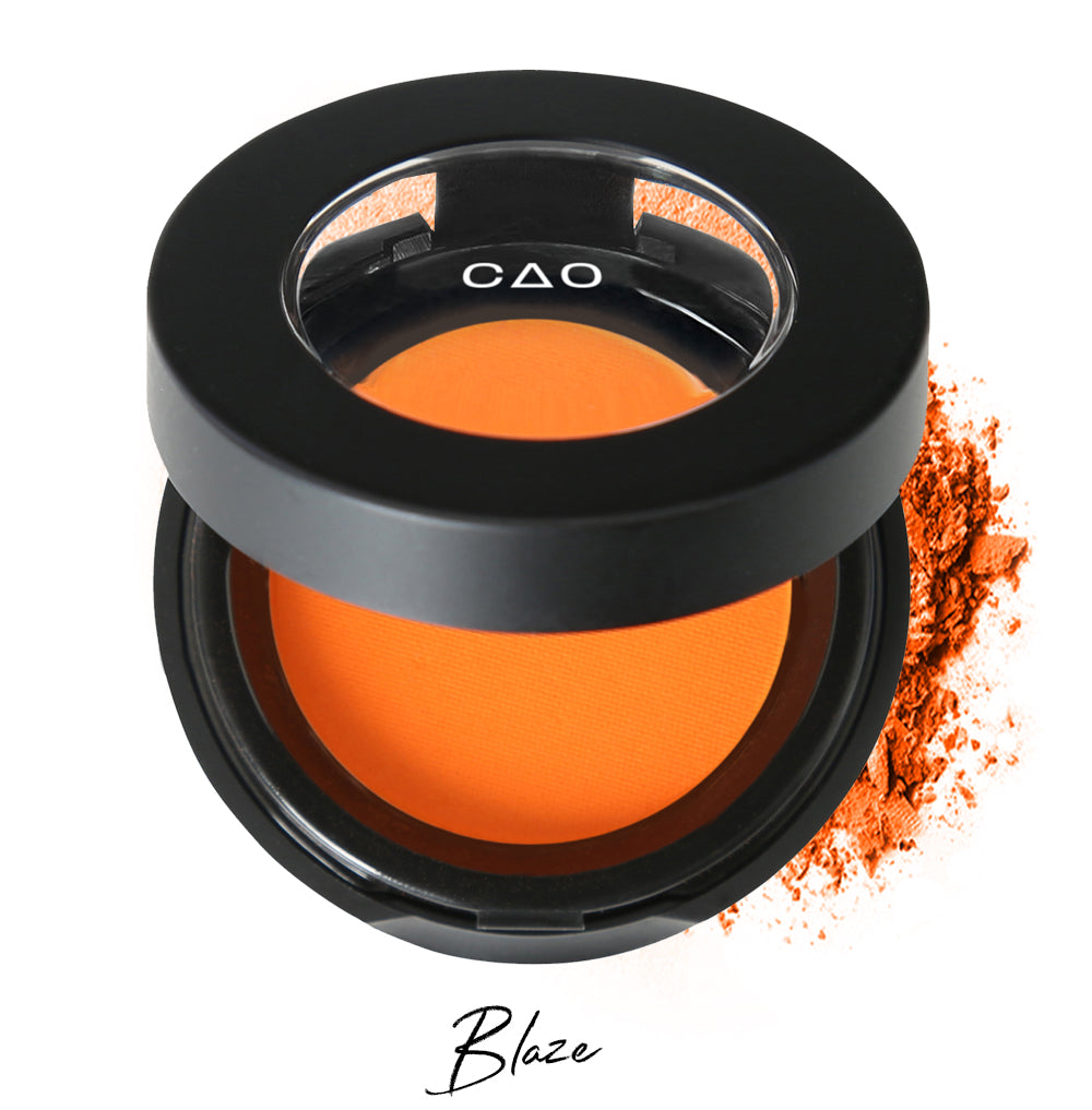 Semi- open eyeshadow compact with neon orange eyeshadow in shade "bliss" compressed powder and on white background with loose eyeshadow powder on white.