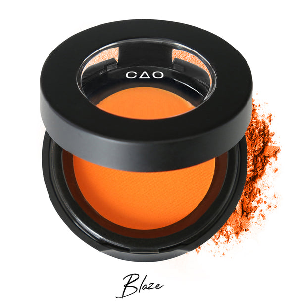 Semi- open eyeshadow compact with neon orange eyeshadow in shade "bliss" compressed powder and on white background with loose eyeshadow powder on white.