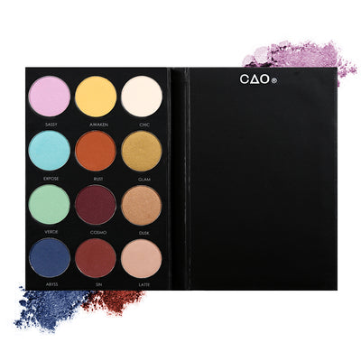 Black eyeshadow pallete with 12 shades of circular compressed eyeshadows. From left to right, First row: pink, light yellow, cream. Second Row: teal rust, mustard, third row: seafoam, burgundy, light brown. Last Row: dark blue, rust, light nude.