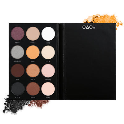 Black eyeshadow pallete with 12 shades of circular compressed eyeshadows. From left to right, First row:mauve, light brown, white. Second Row: grey, light orange, cream. Third row: dark brown, light brown, light pink. Last Row: charcoal, warm brown, light peach