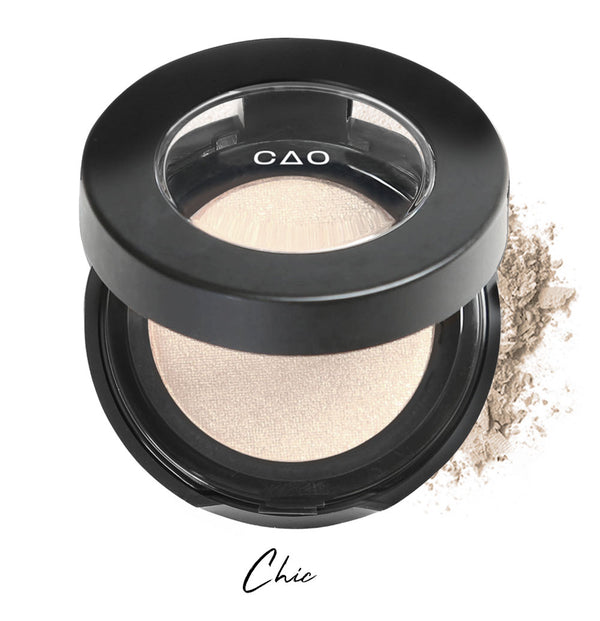 Semi- open eyeshadow compact with almond milk colored eyeshadow in shade "chic" compressed powder and on white background with loose eyeshadow powder on white..