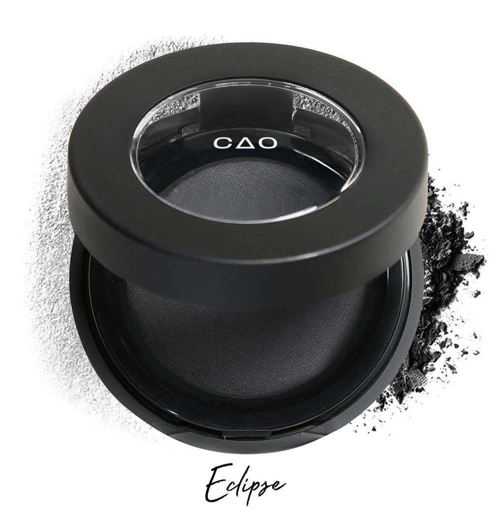 Semi-open eyeshadow compact with biege eyeshadow in shade "demure" compressed powder and on white background with loose eyeshadow powder on white.