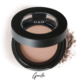 Semi-open eyeshadow compact with beige eyeshadow in shade "gentle" compressed powder and on white background with loose eyeshadow powder on white.