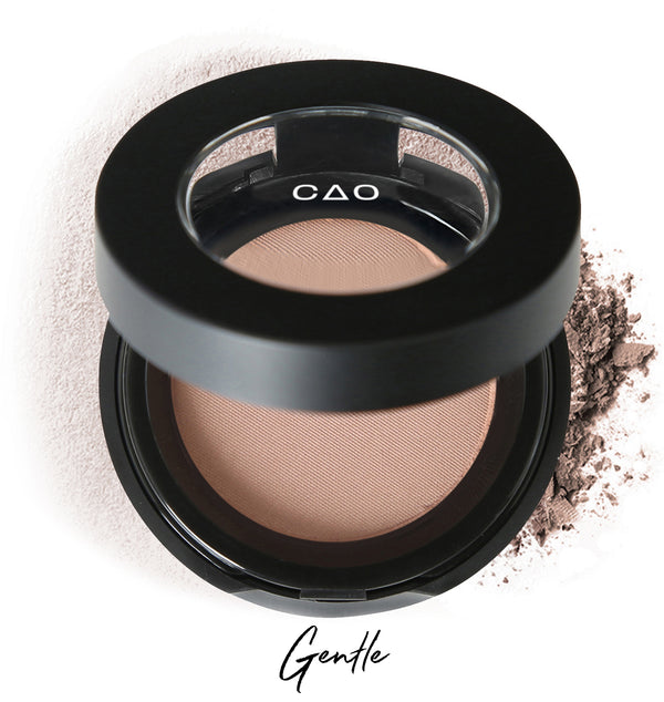 Semi-open eyeshadow compact with beige eyeshadow in shade "gentle" compressed powder and on white background with loose eyeshadow powder on white.