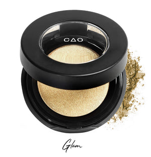 Semi- open eyeshadow compact with light shimmer gold eyeshadow in shade "glam" compressed powder and on white background with loose eyeshadow powder on white..