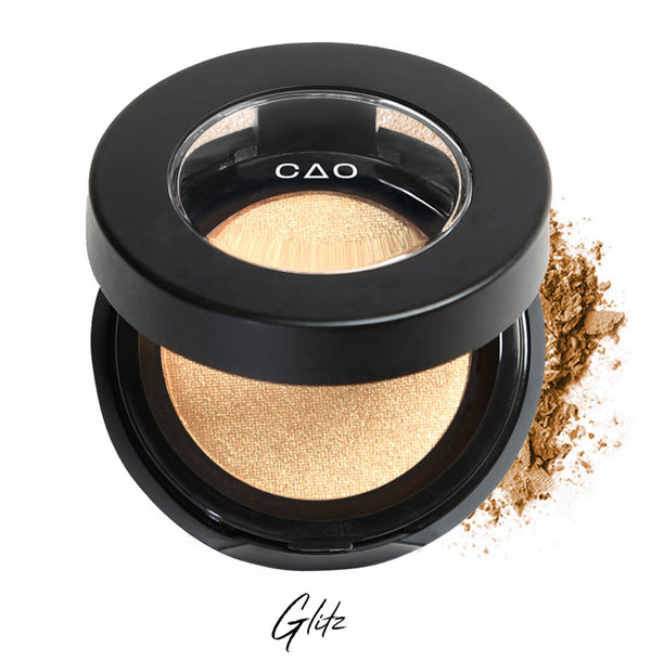 Semi- open eyeshadow compact with shimmer warm gold eyeshadow in shade "Glitz" compressed powder and on white background with loose eyeshadow powder on white..