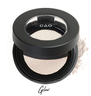 Semi-open eyeshadow compact with white eyeshadow in shade "glow" compressed powder and on white background with loose eyeshadow powder on white.