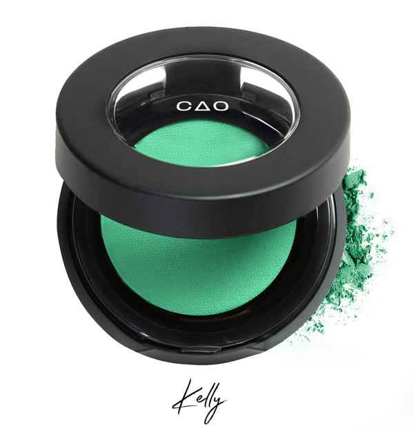 Semi- open eyeshadow compact with light neon green eyeshadow in shade "Kelly" compressed powder and on white background with loose eyeshadow powder on white..
