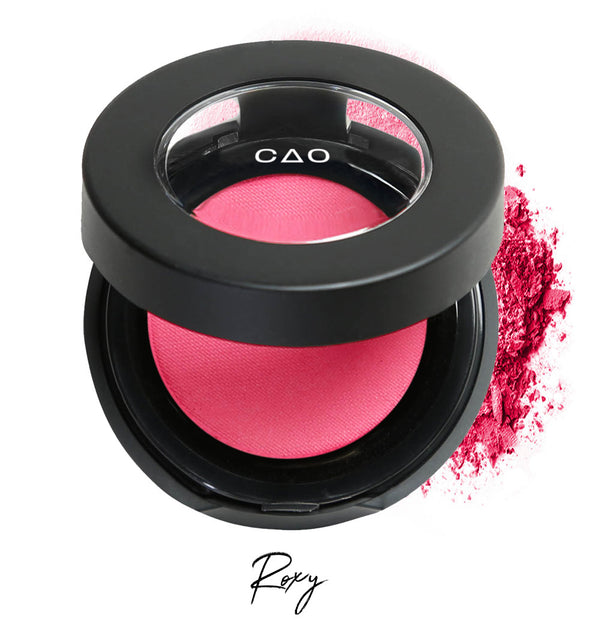 Semi- open eyeshadow compact with neon pink eyeshadow in shade "Roxy" compressed powder and on white background with loose eyeshadow powder on white..