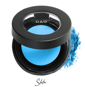 Semi- open eyeshadow compact with light neon blue eyeshadow in shade "Slate" compressed powder and on white background with loose eyeshadow powder on white..