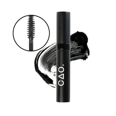 Closeup image of mascara wand tip and bristles in a black lined circle on left, on white Black matte with shiny ring mascara tube, on top of black mascara swatch on background. 