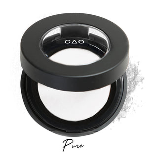 Semi-open eyeshadow compact with white eyeshadow in shade "pure" compressed powder and on white background with loose eyeshadow powder on white.