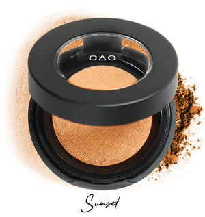Semi- open eyeshadow compact with light orange eyeshadow in shade "sunset" compressed powder and on white background with loose eyeshadow powder on white.
