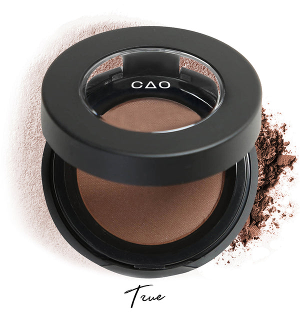 Semi-open eyeshadow compact with brown eyeshadow in shade "true" compressed powder and on white background with loose eyeshadow powder on white.