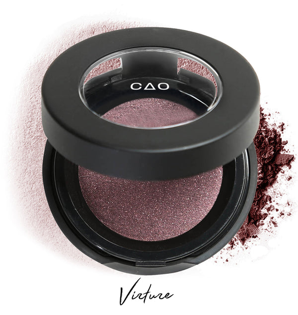 Semi-open eyeshadow compact with mauve eyeshadow in shade "virtue" compressed powder and on white background with loose eyeshadow powder on white.